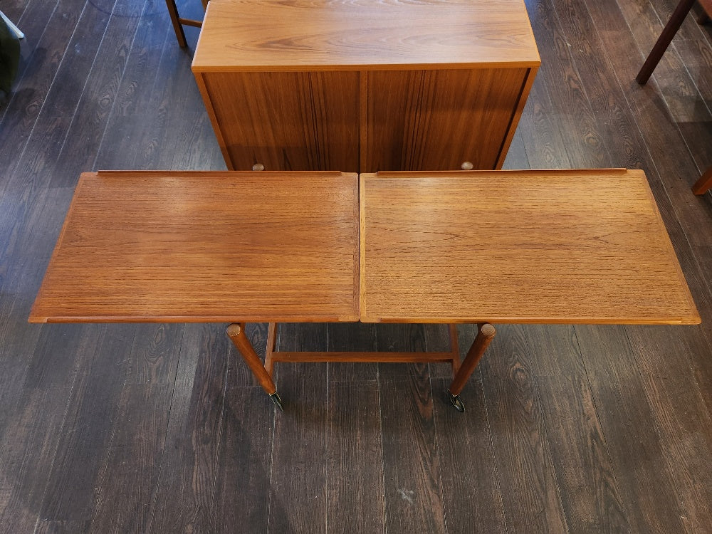 Absolutely fabulous 1960s extending teak tea cart with flared edge. Extend the two level cart to a longer serving cart by sliding the top shelf over and clicking the bottom shelf into place beside it. Original casters. Attributed to Danish furniture maker Poul Hundevad. Expanded with bottom shelf.- Cook Street Vintage