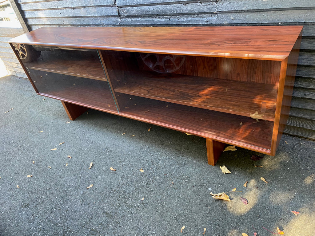 Wonderful 1960s teak sideboard. Incredible grain. Two glass sliding doors, two adjustable height shelves and solid square legs. Perfect for a display case or sideboard- Cook Street Vintage.