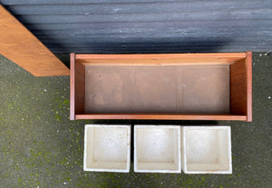 Top view with styrofoam inserts removed and on ground. The perfect touch for any room. The original styrofoam inserts accommodate three medium-sized plants. Makeshift wood lid that can transform this unit into a small side table or storage bin- Cook Street Vintage