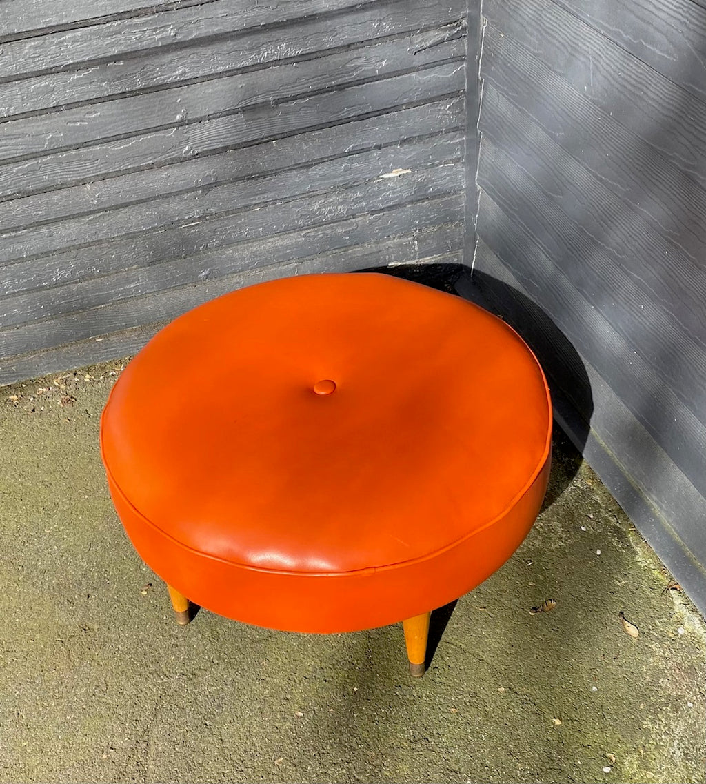 Classic round four leg round foot stool in orange. Tapered legs with brass caps. Centre button detail on cushion- Cook Street Vintage.
