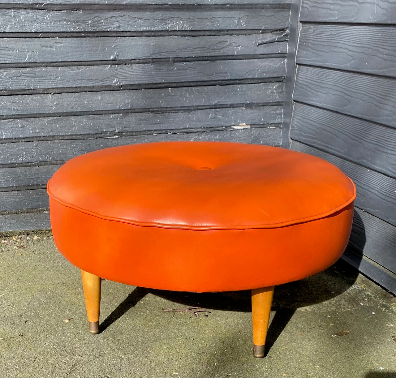 Classic round four leg round foot stool in orange. Tapered legs with brass caps. Centre button detail on cushion- Cook Street Vintage.