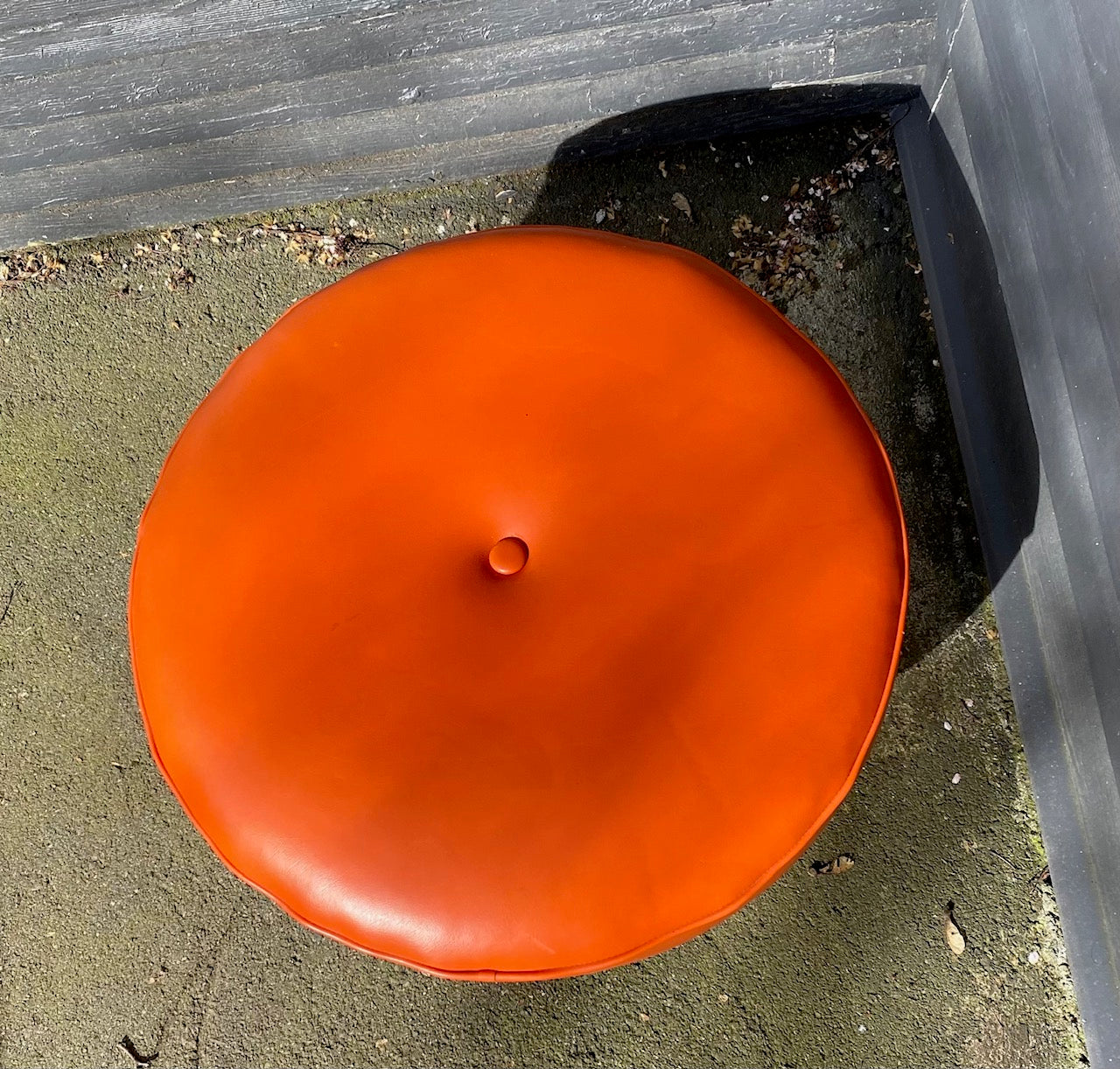 Classic mid-century round four leg round hassock in orange. Tapered legs with brass caps. Centre button detail on cushion- Cook Street Vintage.