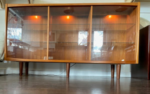 Whether to showcase your midcentury barware, vintage glassware or ceramic collection, your china or books, this gorgeous Danish designed glass front cabinet has perfect lighting to create a stunning display. Three sliding glass doors with teak trim open to adjustable height glass shelves. Subtle arch top curtain. Made in Denmark by Laurits M Larsen Mobelfabrik.- Cook Street Vintage