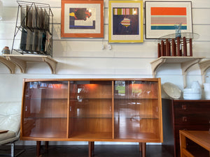 Whether to showcase your midcentury barware, vintage glassware or ceramic collection, your china or books, this gorgeous Danish designed glass front cabinet has perfect lighting to create a stunning display. Three sliding glass doors with teak trim open to adjustable height glass shelves. Subtle arch top curtain. Made in Denmark by Laurits M Larsen Mobelfabrik with empty glass shelves- Cook Street Vintage