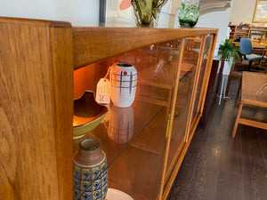 Whether to showcase your midcentury barware, vintage glassware or ceramic collection, your china or books, this gorgeous Danish designed glass front cabinet has perfect lighting to create a stunning display. Three sliding glass doors with teak trim open to adjustable height glass shelves. Subtle arch top curtain. Made in Denmark by Laurits M Larsen Mobelfabrik.- Cook Street Vintage
