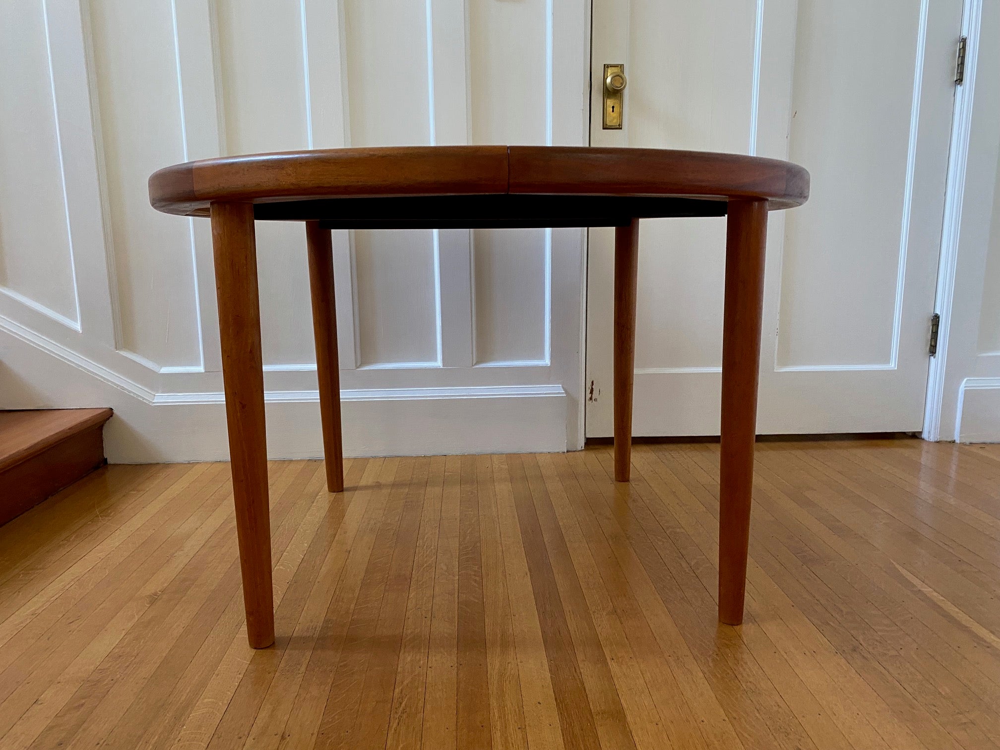 Side view on Gorgeous Mid-century honey teak round dining table. Smaller profile than our other round dining tables, this beauty has an elegant staved edge of solid teak- Cook Street Vintage