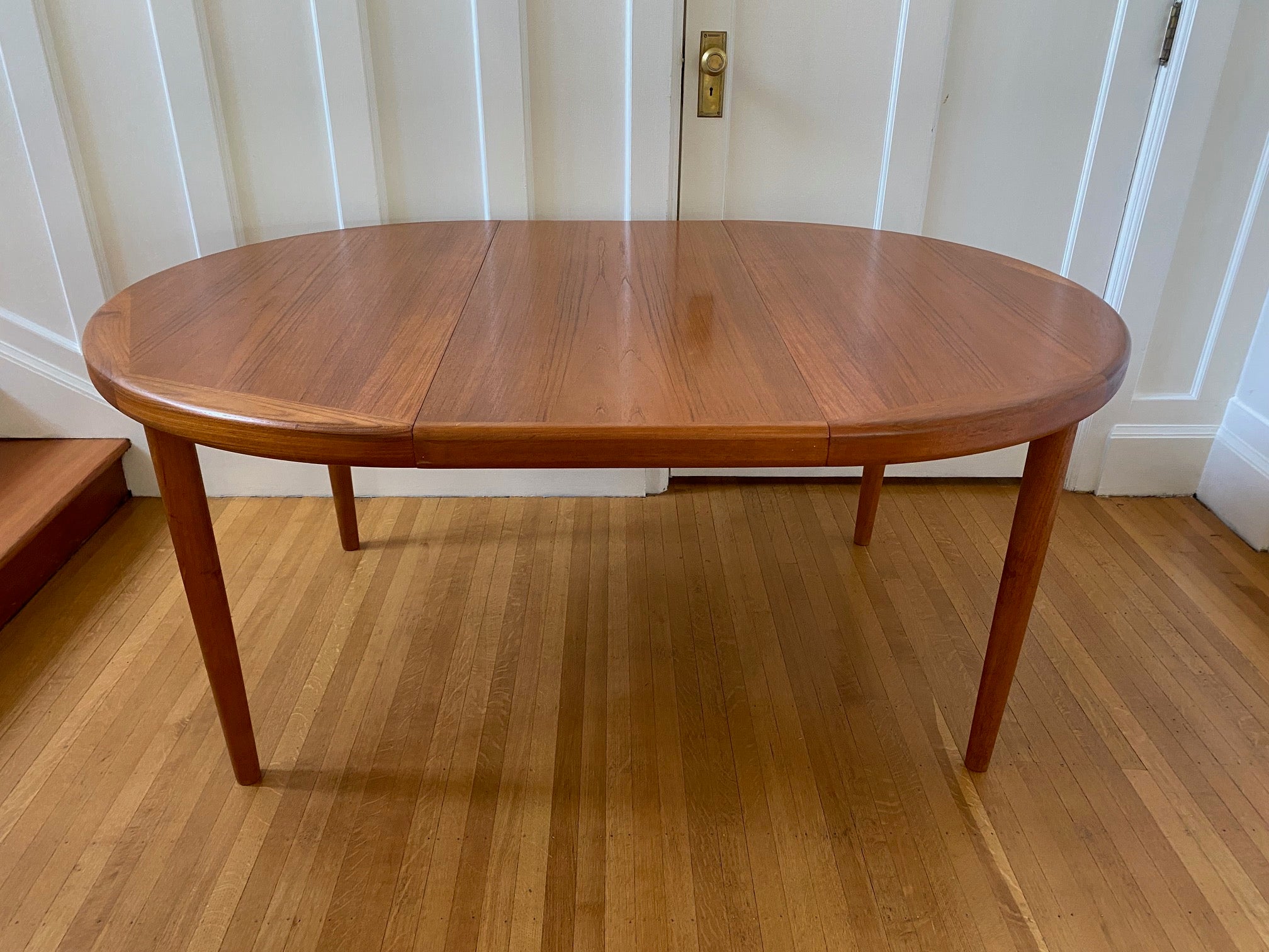 Top view of table with one leaf in of Gorgeous Mid-century honey teak round dining table. Smaller profile than our other round dining tables, this beauty has an elegant staved edge of solid teak- Cook Street Vintage