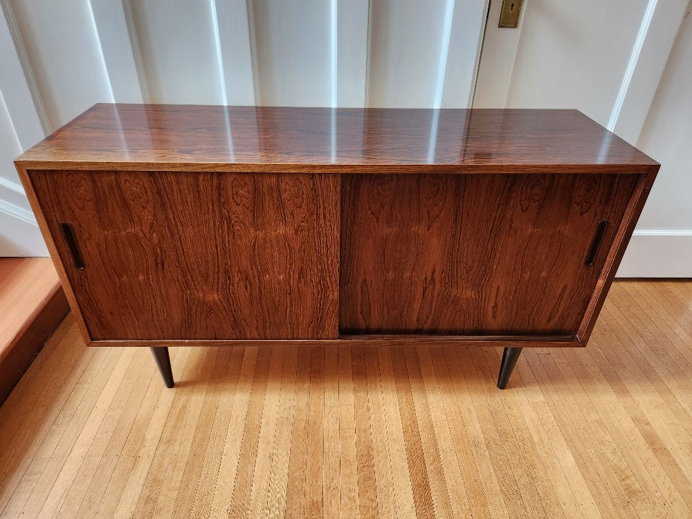 Beautiful Danish rosewood sideboard. Sliding cabinet doors with adjustable interior shelves. One felt lined hidden drawer. Made in Denmark by Poul Dogvad for Hundevad & Co- Cook Street Vintage