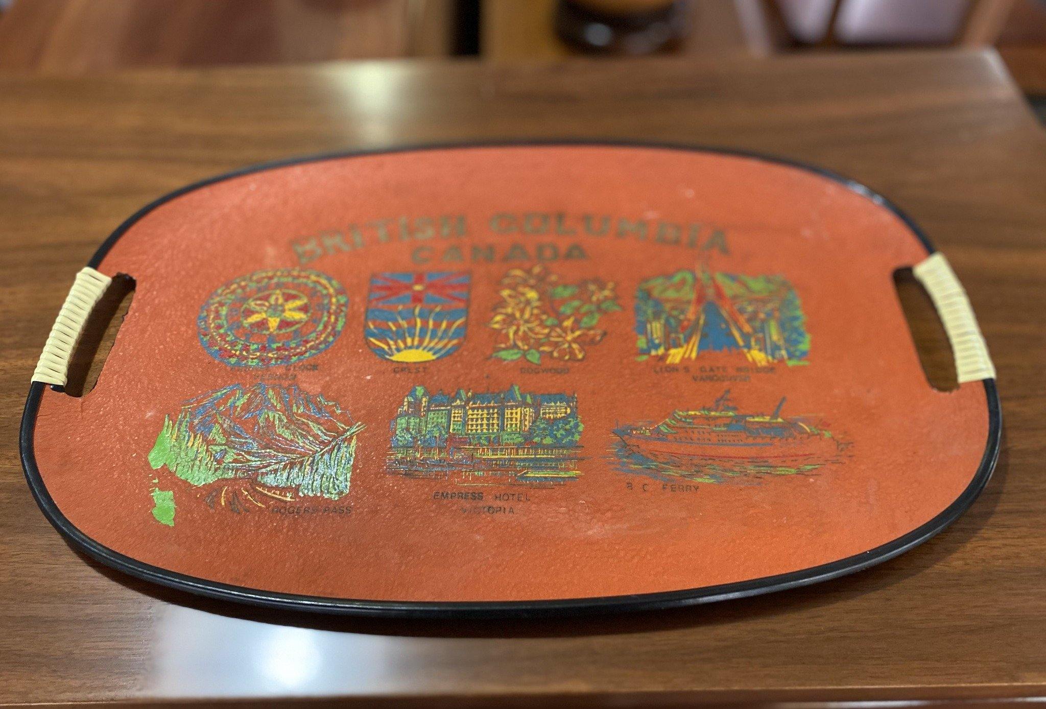 Orange BC souvenir tray with white plastic wrapped handles and images of Empress Hotel, BC Ferry, BC Crest, Rogers Pass- Cook Street Vintage